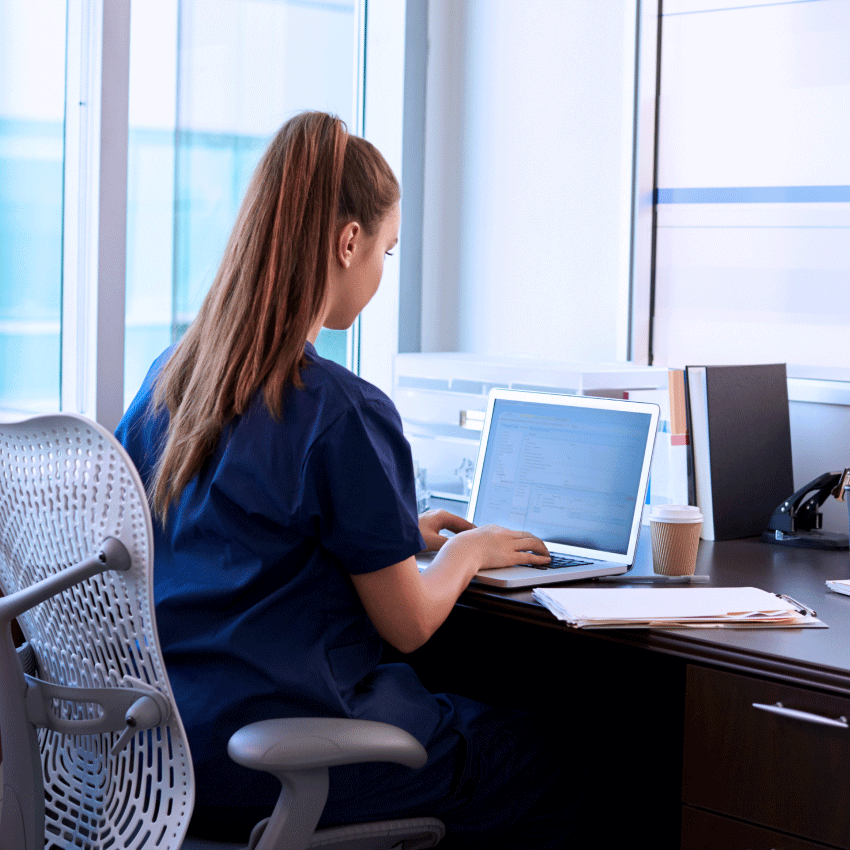 Female nurse wearing scrubs using laptop computer.