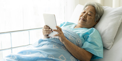 Patient in hospital bed reading from a digital tablet