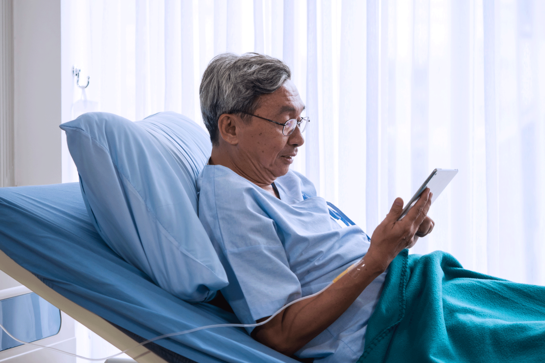 Male patient sitting up in hospital bed using a tablet device.