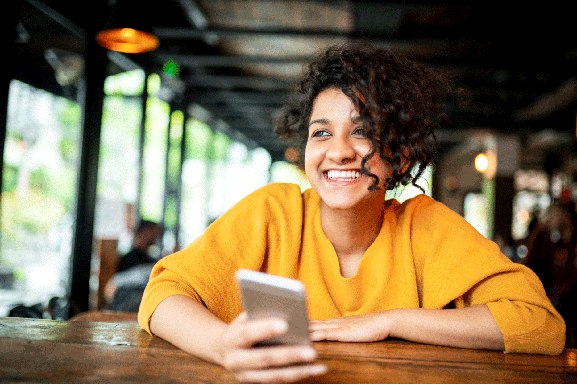 Smiling woman wearing a yellow t-shirt holding a mobile phone.
