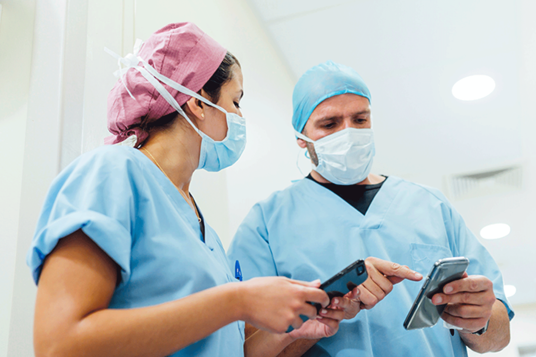 Male and female clinician in surgery scrubs looking at their mobile phones.