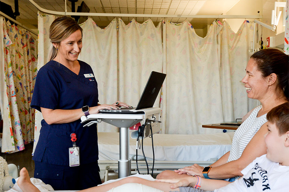 Female nurse standing beside a female patient and young child in hospital bed.
