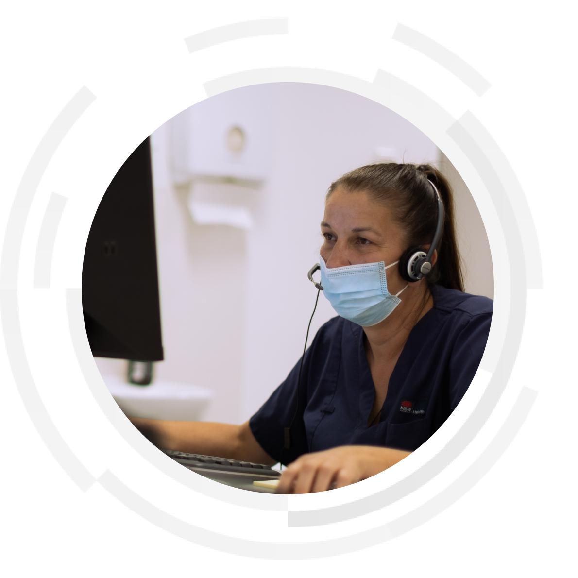 Female nurse wearing a mask and headset looking at computer monitor.