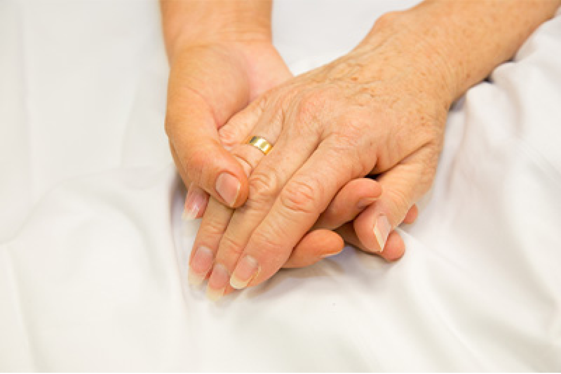 Two hands clasped together on a hospital bed.