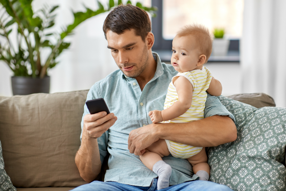 Father holding his baby and using mobile phone at the same time