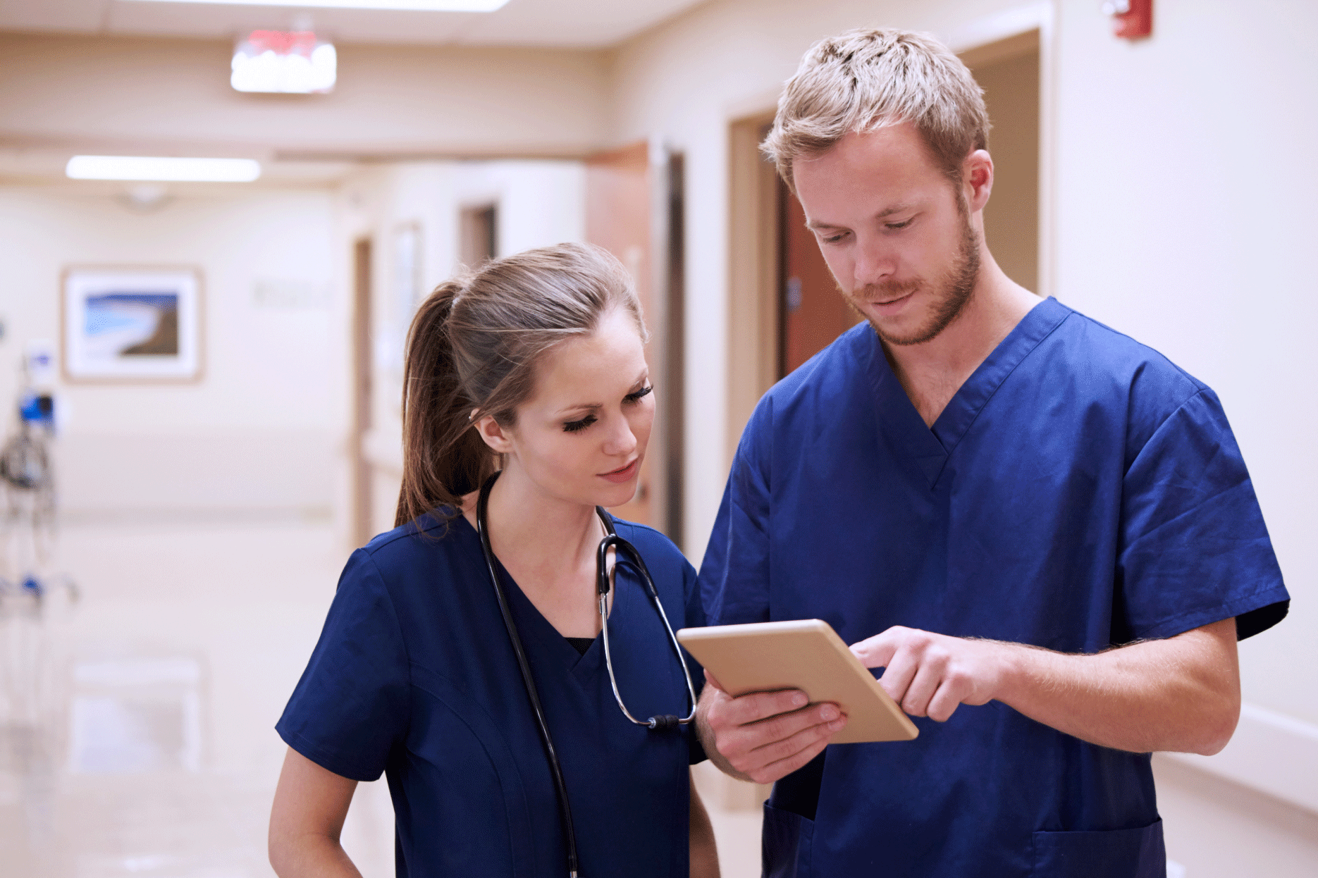 Two clinicians standing in hospital hallway looking at tablet screen.