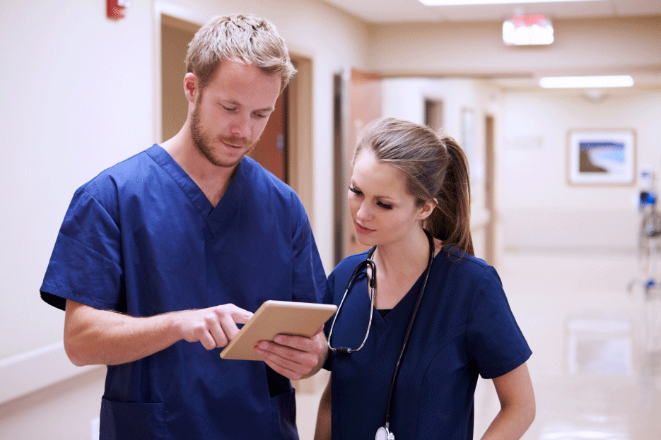 Two clinicians in a hospital hallway looking at a tablet device