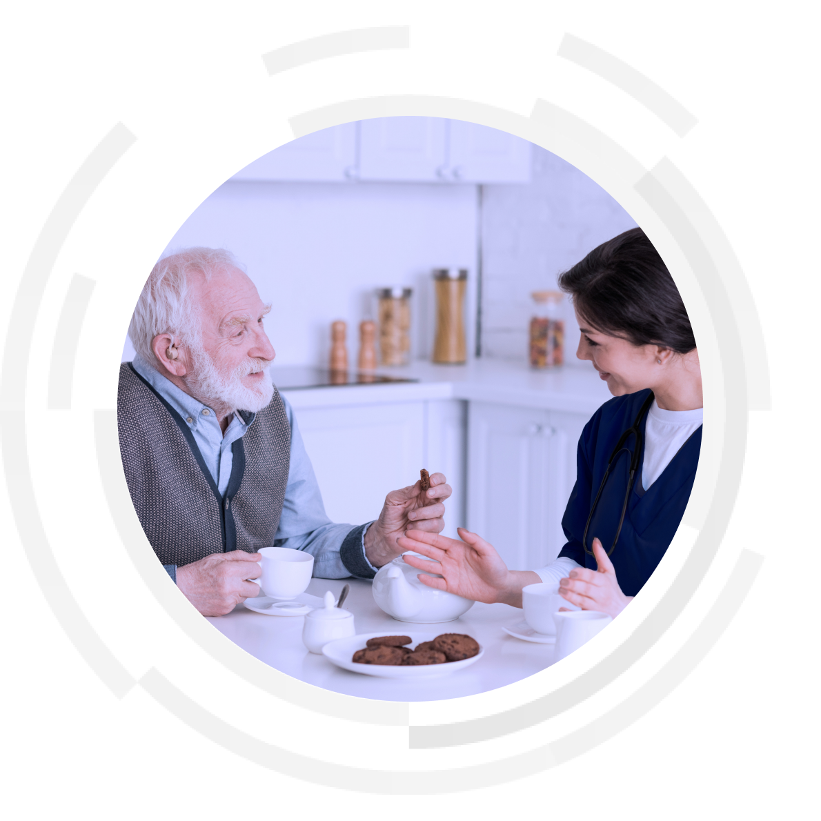 Elderly patient and nurse sitting at dining table sharing tea and biscuits.