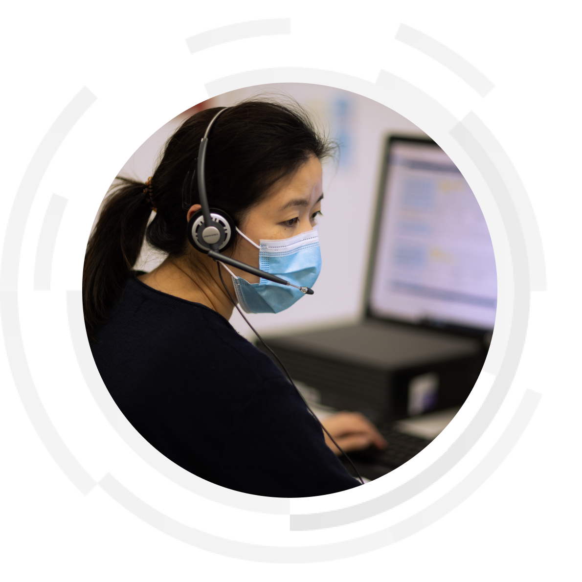 Nurse wearing headset and mask sitting at computer desk.