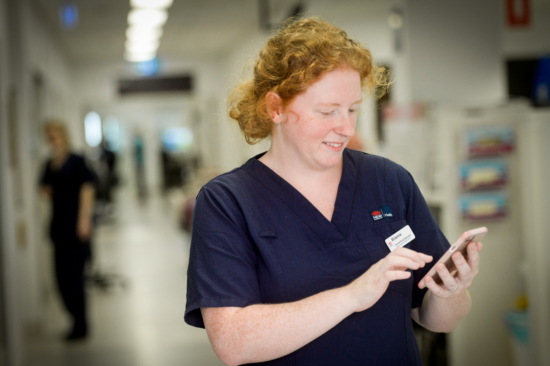 Female nurse checking her mobile phone in a hospital hallway.