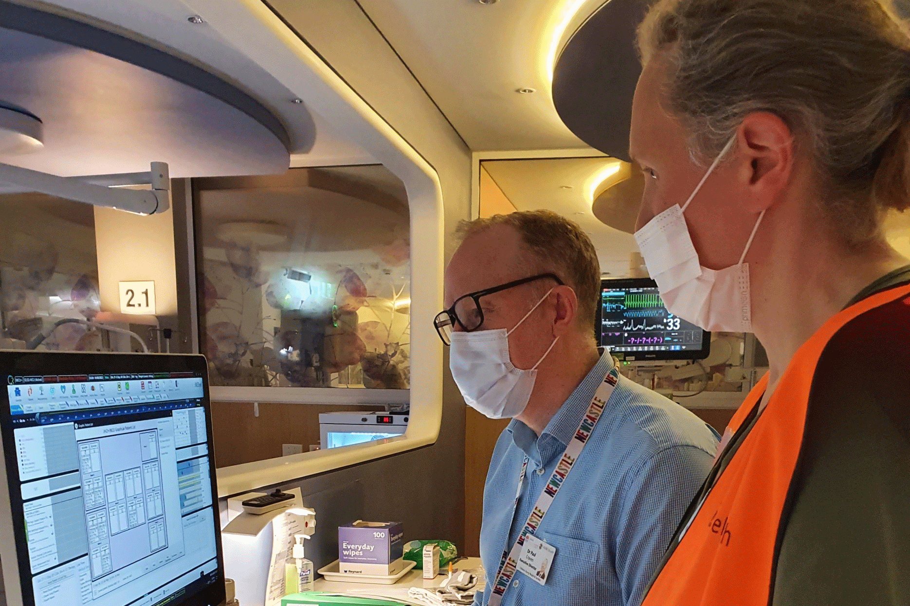 Two male colleagues wearing masks looking at a computer monitor.